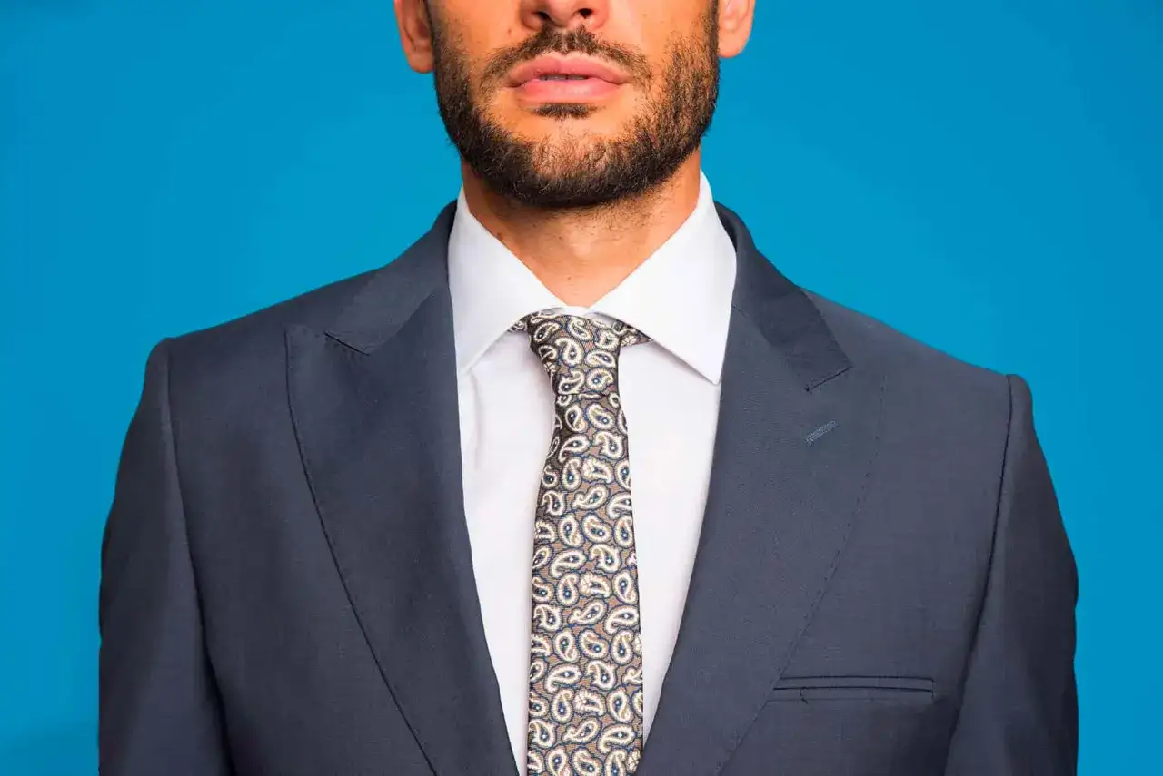 Uomo con abito grigio scuro, camicia bianca e cravatta con fantasia paisley.