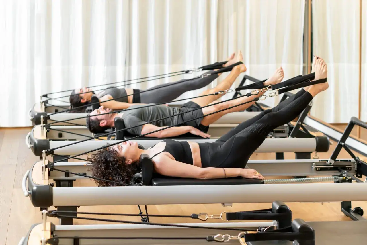 Trzy osoby ćwiczą na reformerach. To świetny sposób, by dowiedzieć się, pilates co to jest i jak poprawić kondycję.