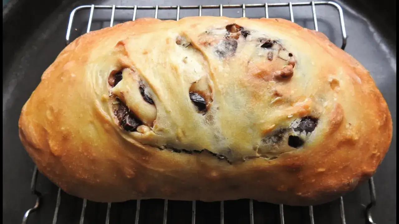 Pan italiano casero con aceitunas negras, recién horneado y enfriándose en una rejilla.