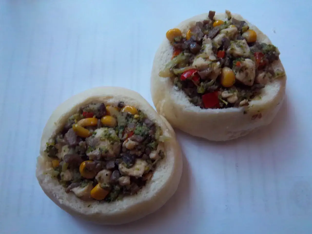 Dwa okrągłe kluski na parze na słono, wypełnione farszem z kurczaka, brokułów, kukurydzy i papryki.