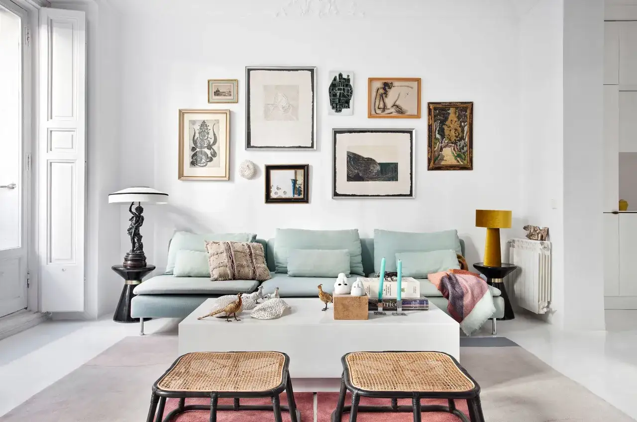 Sal&oacute;n moderno con sof&aacute; azul claro, mesa de centro blanca y una pared llena de cuadros, ideal para aprender como colgar un cuadro.