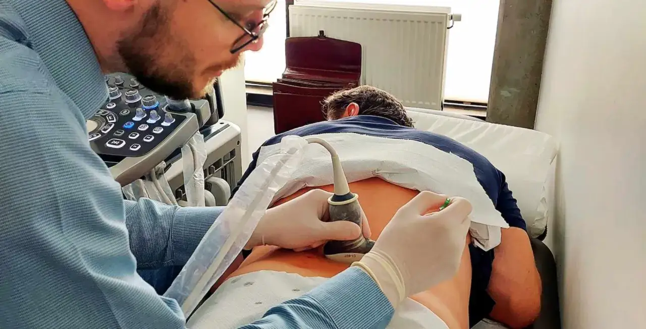 Lekarz wykonuje punkcję pod kontrolą USG. Pacjent leży na brzuchu, lekarz z rękawiczkach przykłada głowicę aparatu do jego pleców.