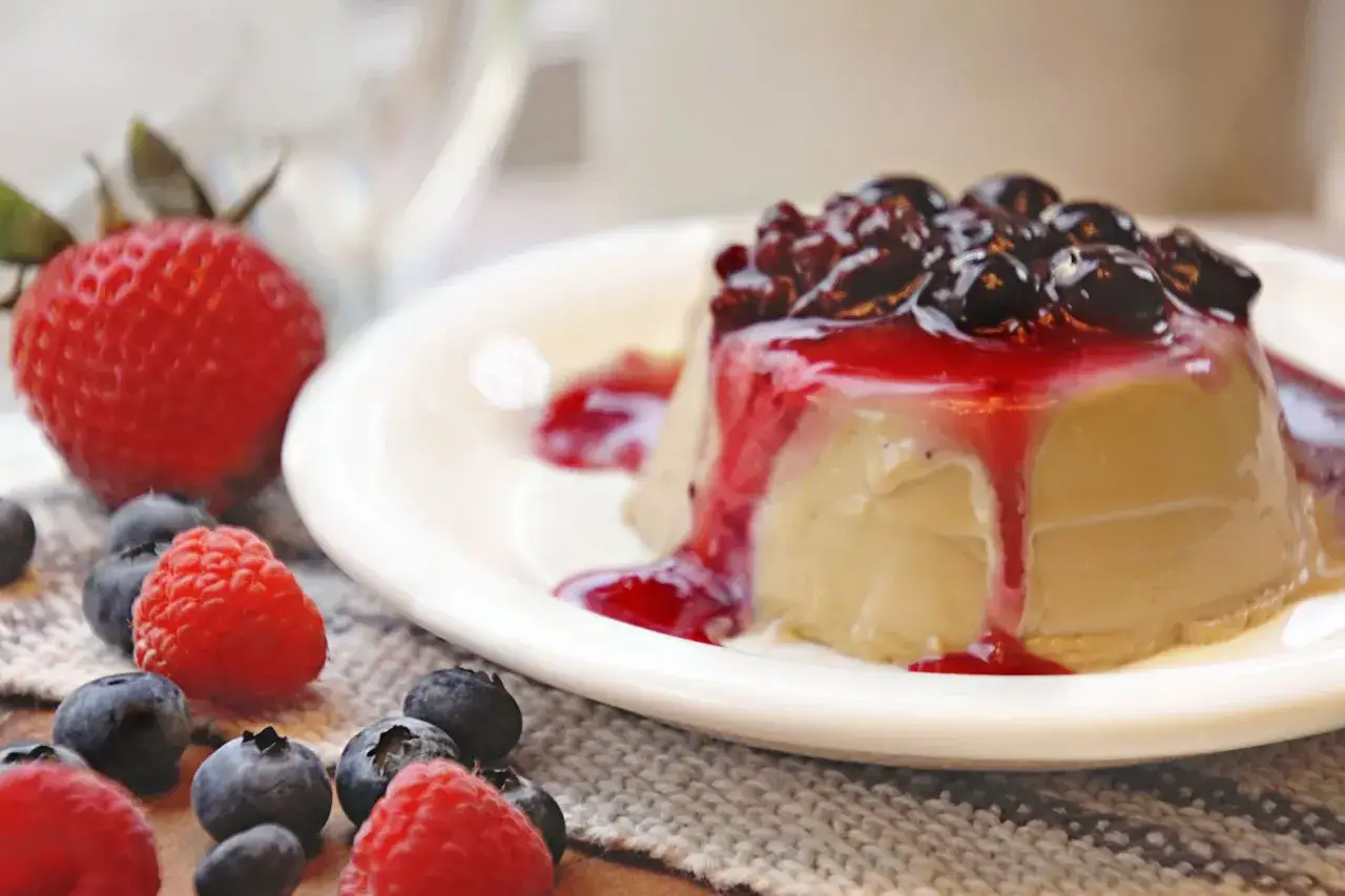 Cremige Panna Cotta mit Beerensoße und frischen Früchten wie Erdbeeren, Himbeeren und Blaubeeren.