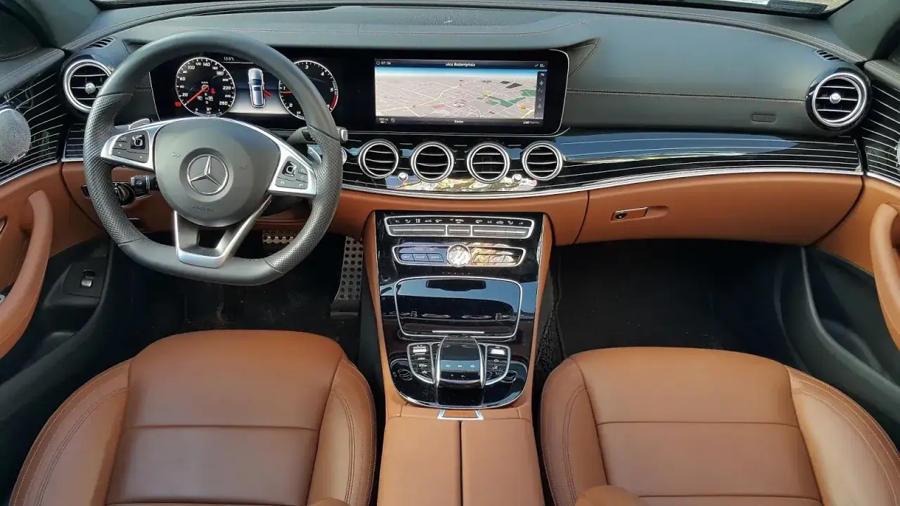 Wnętrze mercedesa w 213 z brązową tapicerką, ekranem nawigacji i kierownicą.