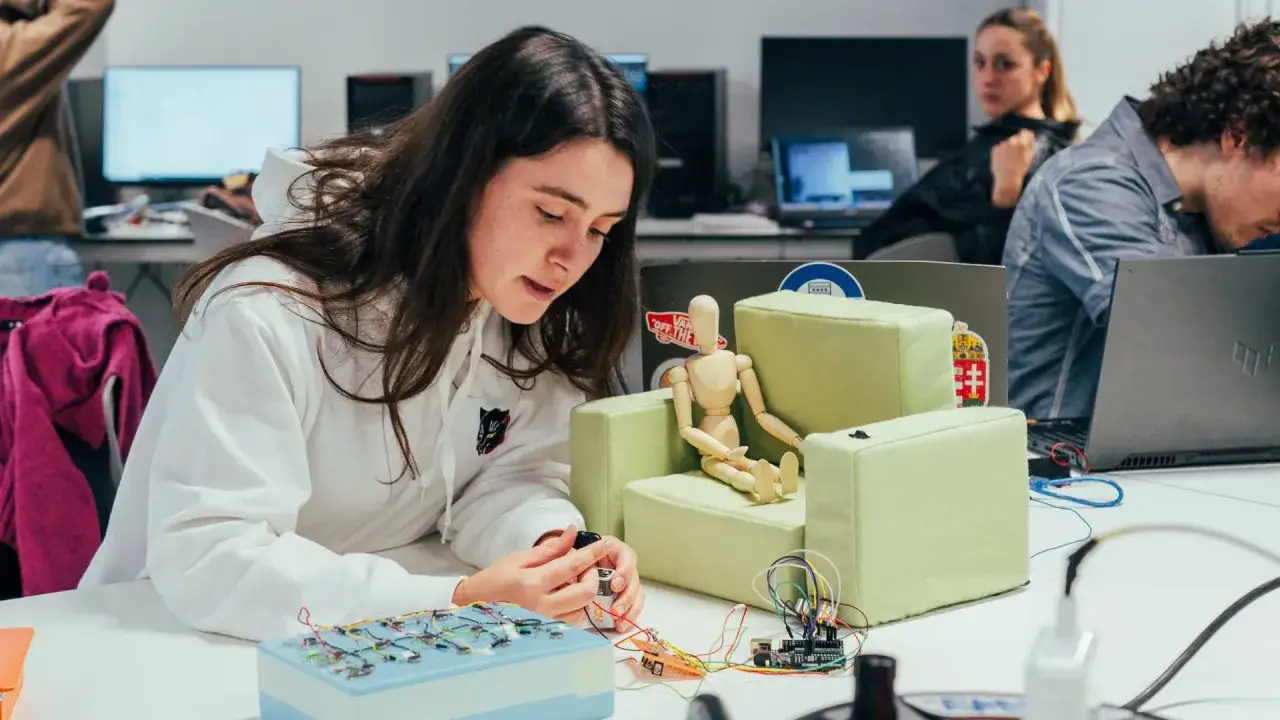 Estudiantes de ingeniería diseño industrial trabajan en un proyecto con circuitos y un maniquí en un aula.