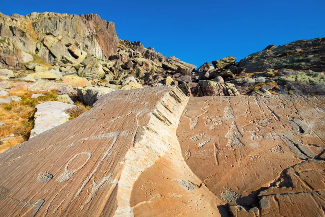 Gravures rupestres préhistoriques sur une roche ocre, dans le décor spectaculaire du parc du Mercantour.
