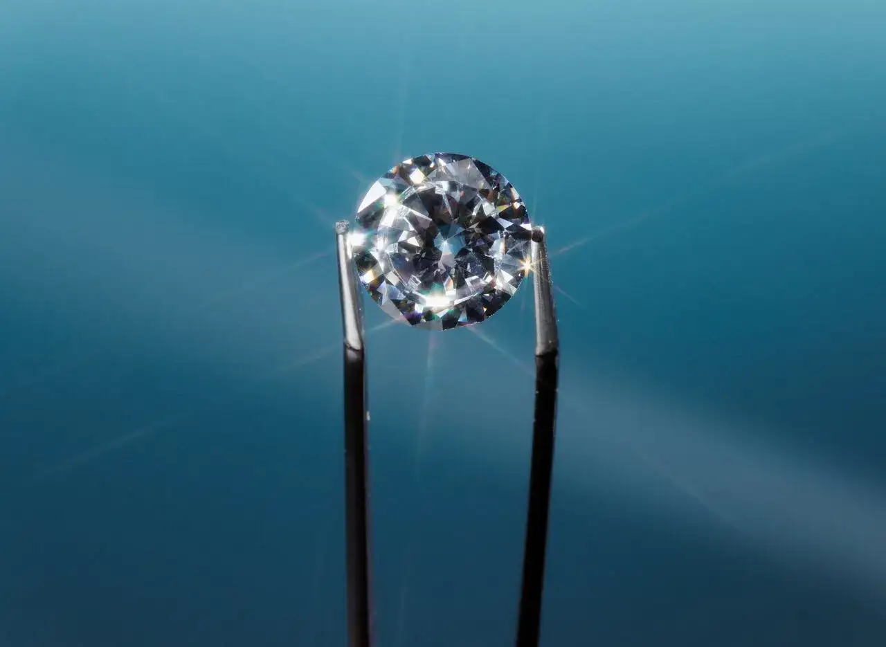 Un deslumbrante diamante real, sujeto por unas pinzas, brilla con destellos bajo la luz sobre un fondo azul.