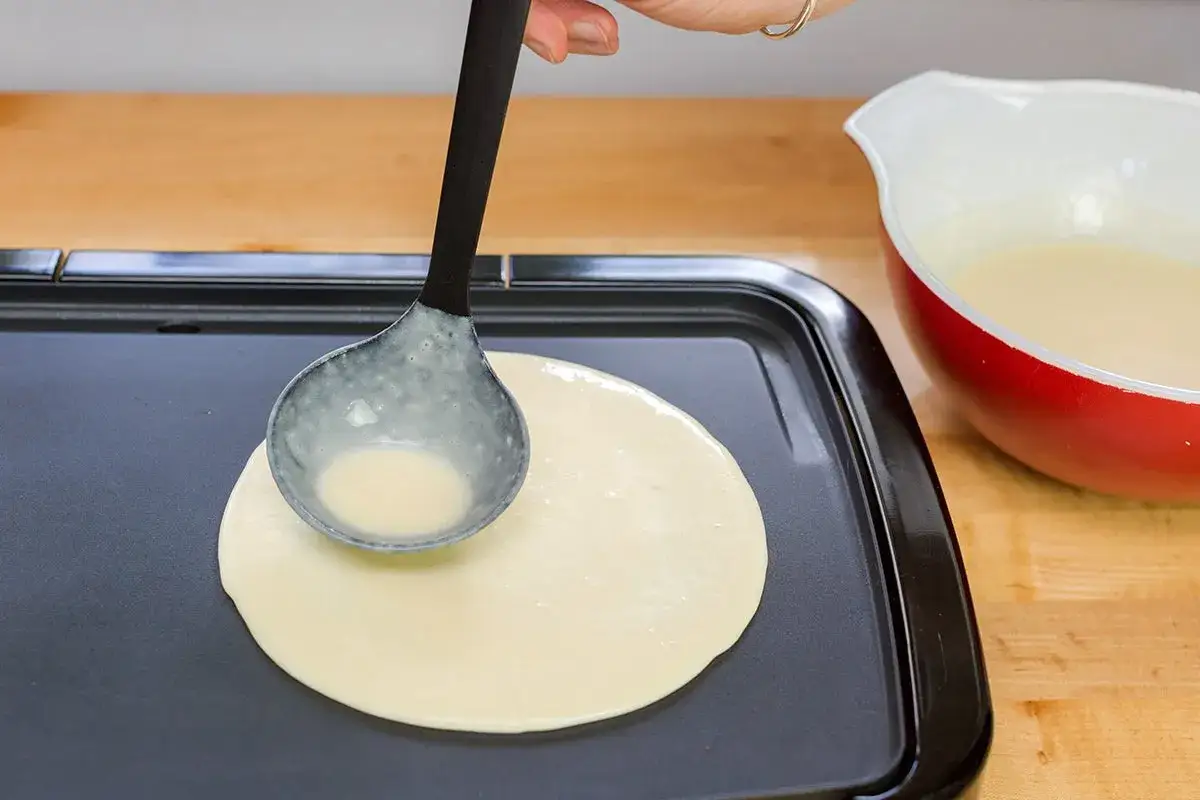 Teig wird mit einer Sch&ouml;pfkelle auf eine hei&szlig;e Platte gegossen, um ein perfektes Pancakes Rezept zu erstellen.