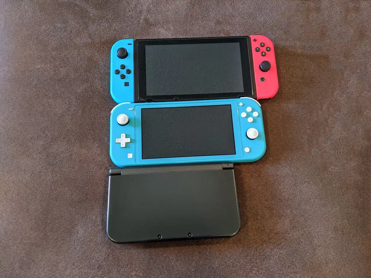 Trzy konsole do gier: niebieski i czerwony Switch, niebieski Switch Lite i czarny 3DS.