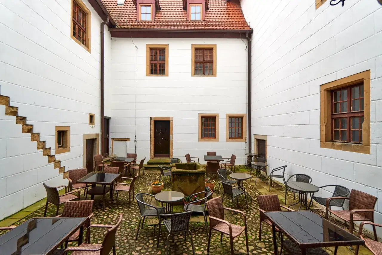 Dziedziniec zamku na wodzie w Wojnowicach z kamienną studnią i stolikami kawiarnianymi.