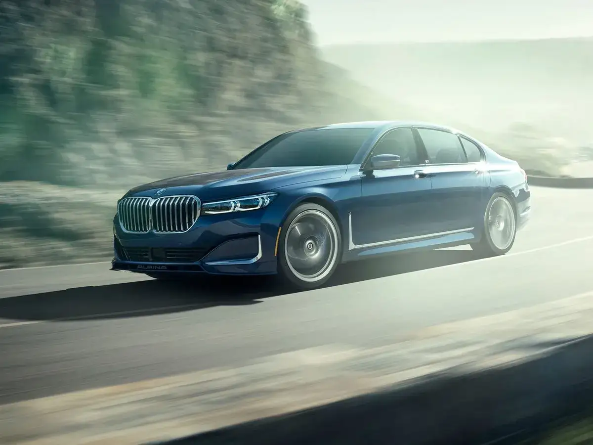 Niebieskie BMW Alpina B7 pędzi po drodze, otoczone rozmytym krajobrazem.