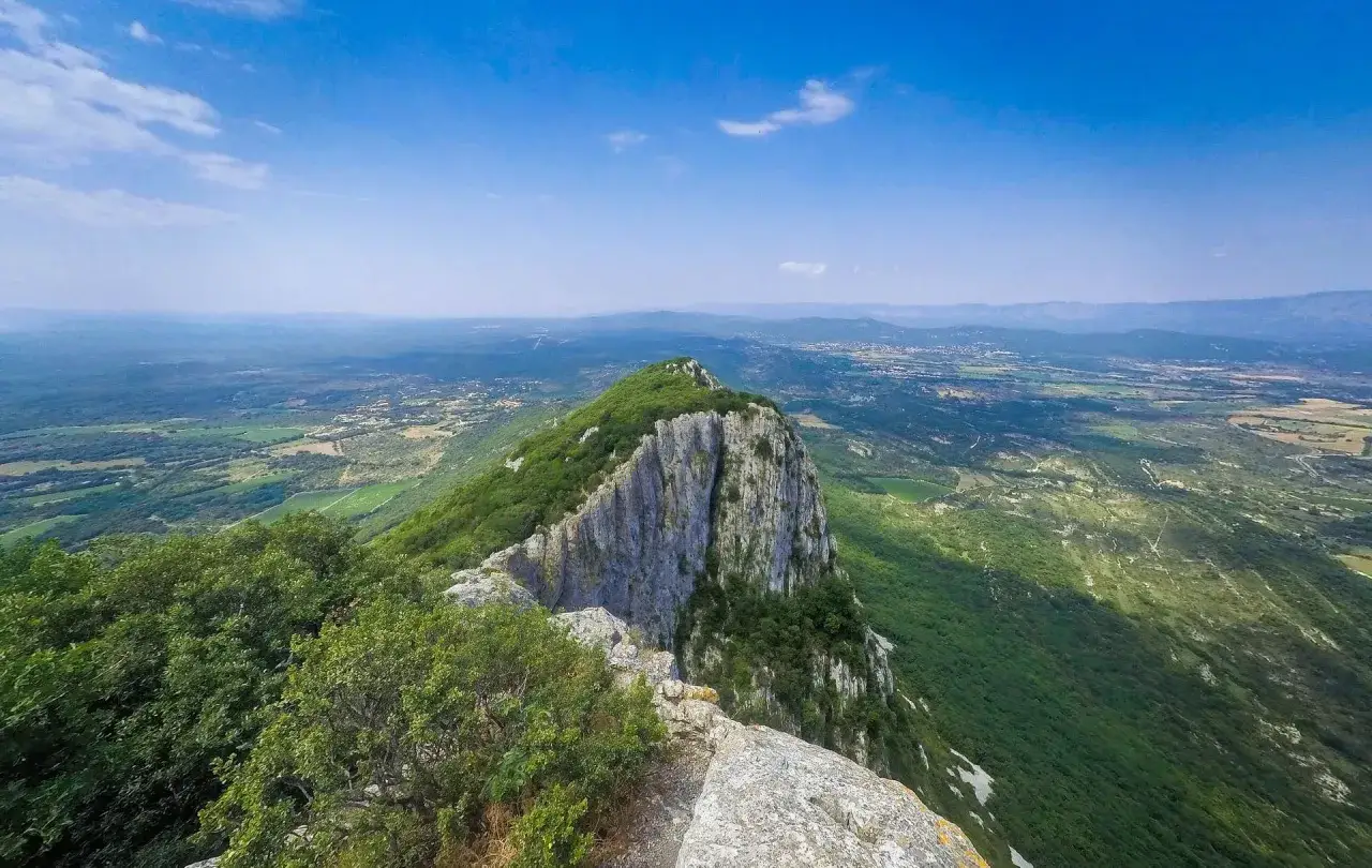 Vue panoramique depuis le pic Saint-Loup, dominant une vallée verdoyante sous un ciel bleu éclatant.