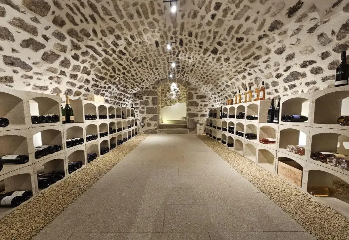 &Eacute;clairage cave &agrave; vin : rang&eacute;es de bouteilles sur des &eacute;tag&egrave;res en b&eacute;ton sous un plafond vo&ucirc;t&eacute; en pierre.
