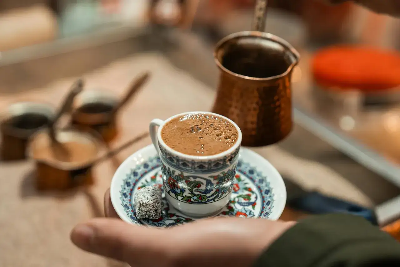 Eine Tasse mit dem besten türkischen Kaffee, verziert mit traditionellen Mustern, daneben ein Stück Lokum. Im Hintergrund eine Kupferkanne.