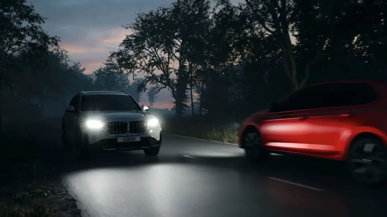 Två bilar kör på en mörk väg. En silverfärgad SUV med starka LED-lampor framför en röd bil. H4 LED godkända lampor lyser upp vägen.
