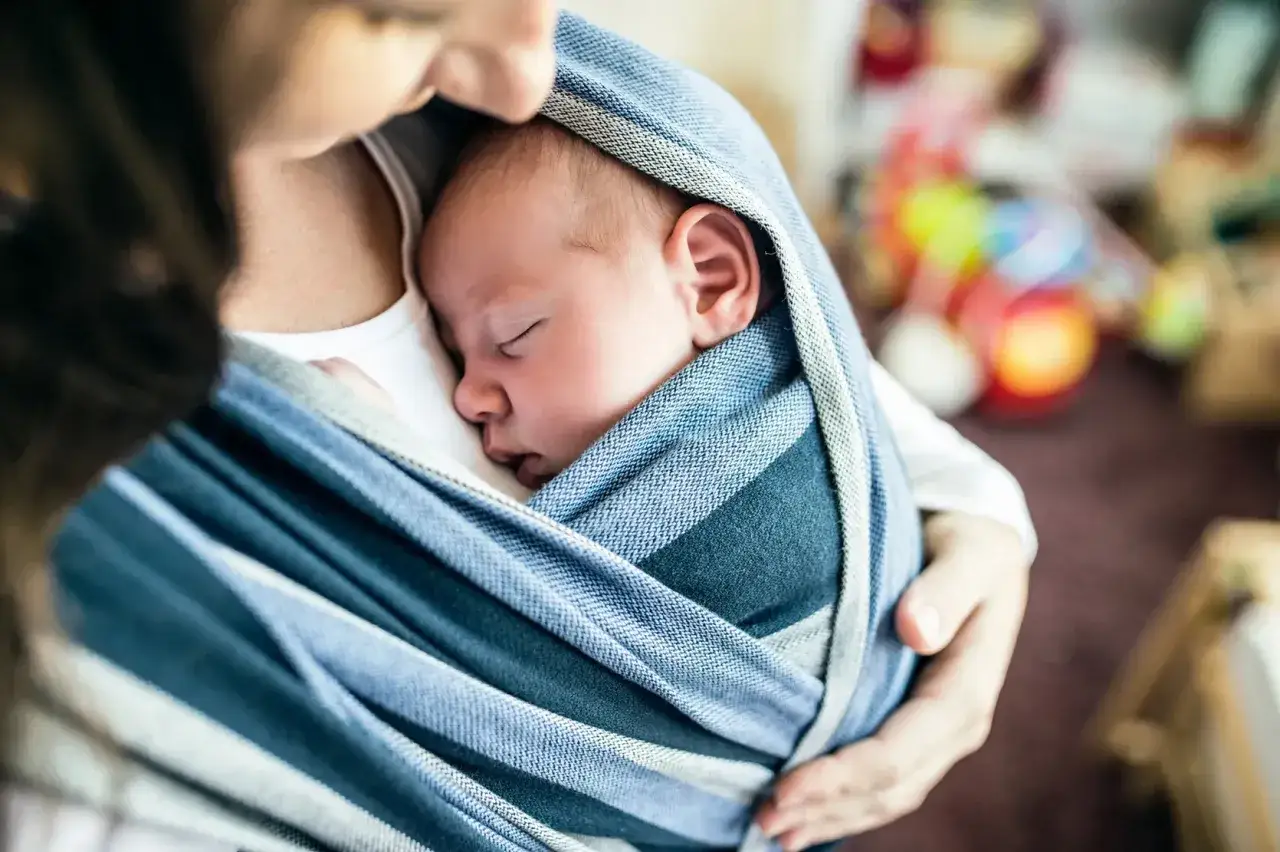 Malutkie dziecko śpi wtulone w chustę. Od kiedy można nosić dziecko w chuście? Od pierwszych dni życia, zapewniając mu bliskość i bezpieczeństwo.