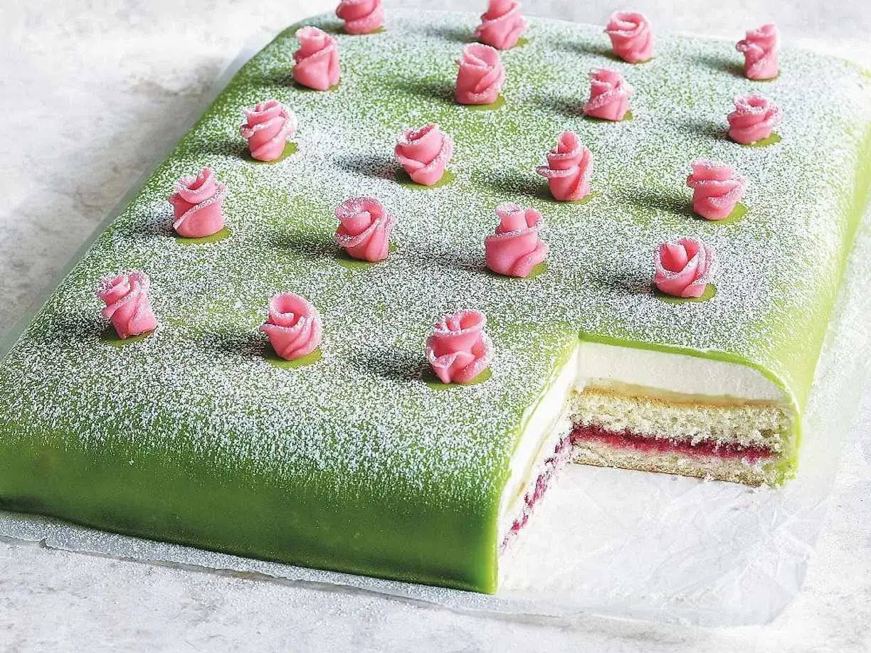 Grön marsipantårta med rosa marsipanrosor och pudersocker, skuren för att visa lager av grädde och sylt. En klassisk tårtbotten långpanna.