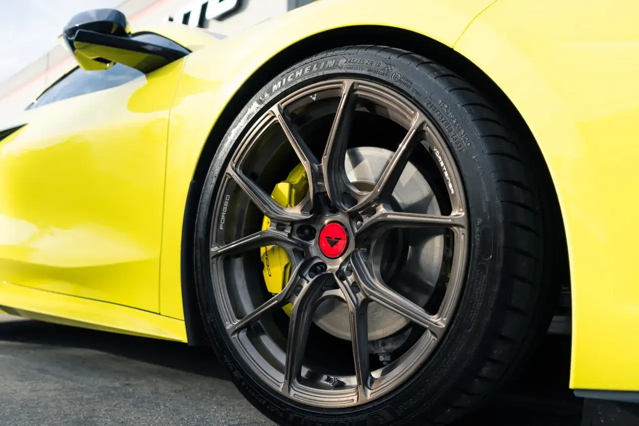Gros plan sur la roue d'une voiture jaune vif, avec un pneu tubeless Michelin et une jante Vorsteiner.