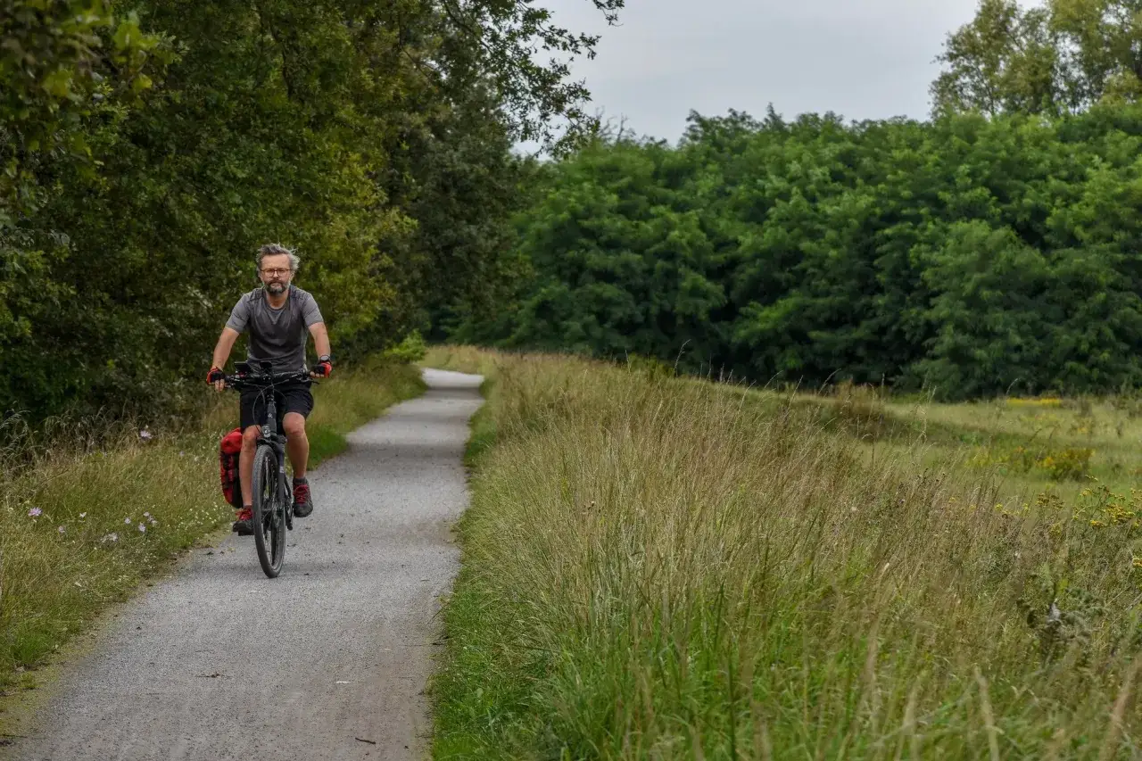 Mężczyzna na rowerze przemierza malownicze trasy rowerowe Wrocławia, otoczony zielenią i wysoką trawą.