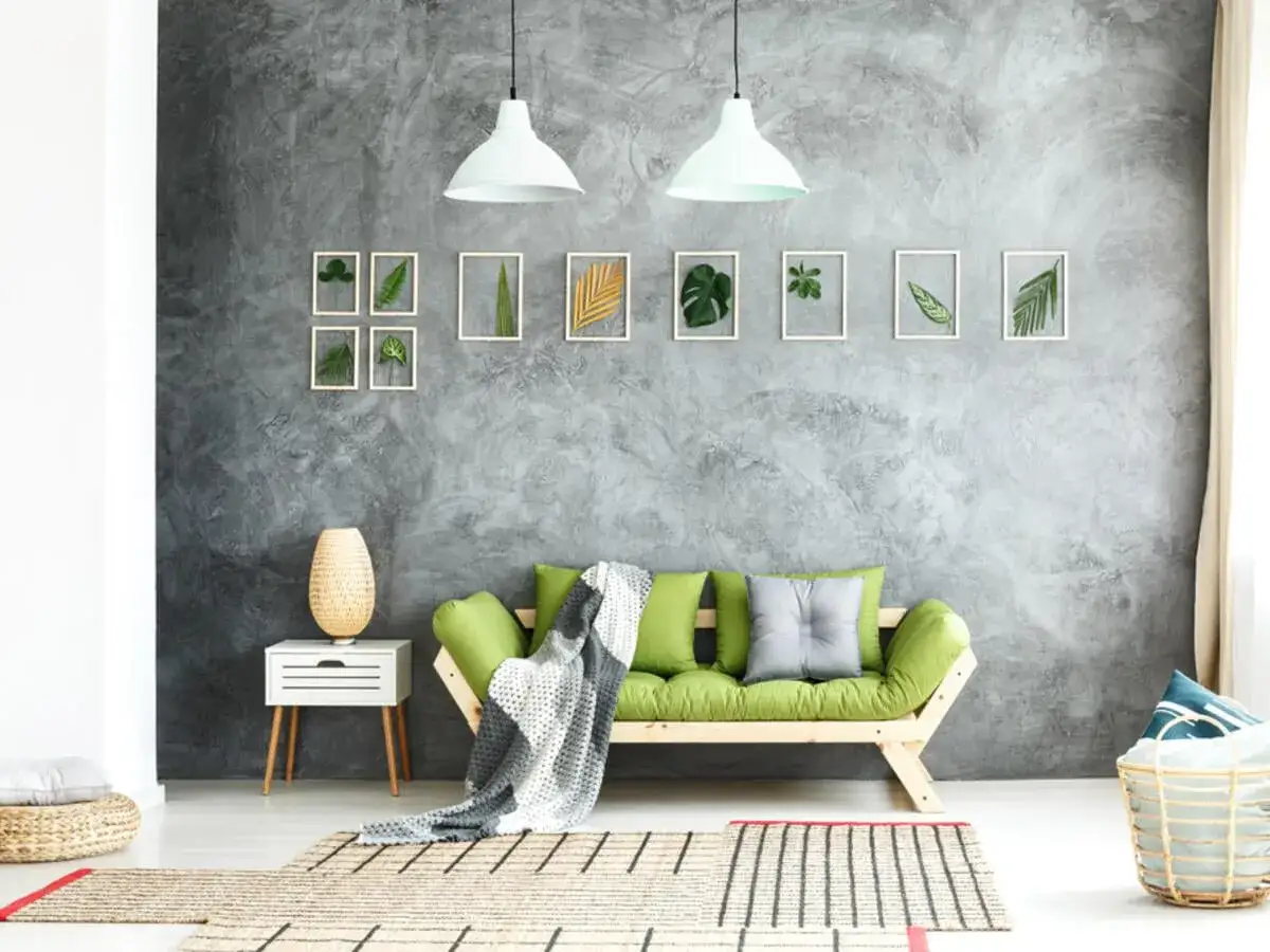 Graue Beton-Struktur Wand mit gerahmten Blättern und einem grünen Sofa.