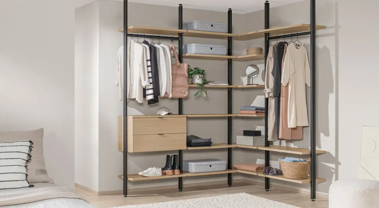 Ein offener Kleiderschrank selber bauen: Holzregale mit Kleidung, Schubladen und Körben an schwarzem Metallgestell.