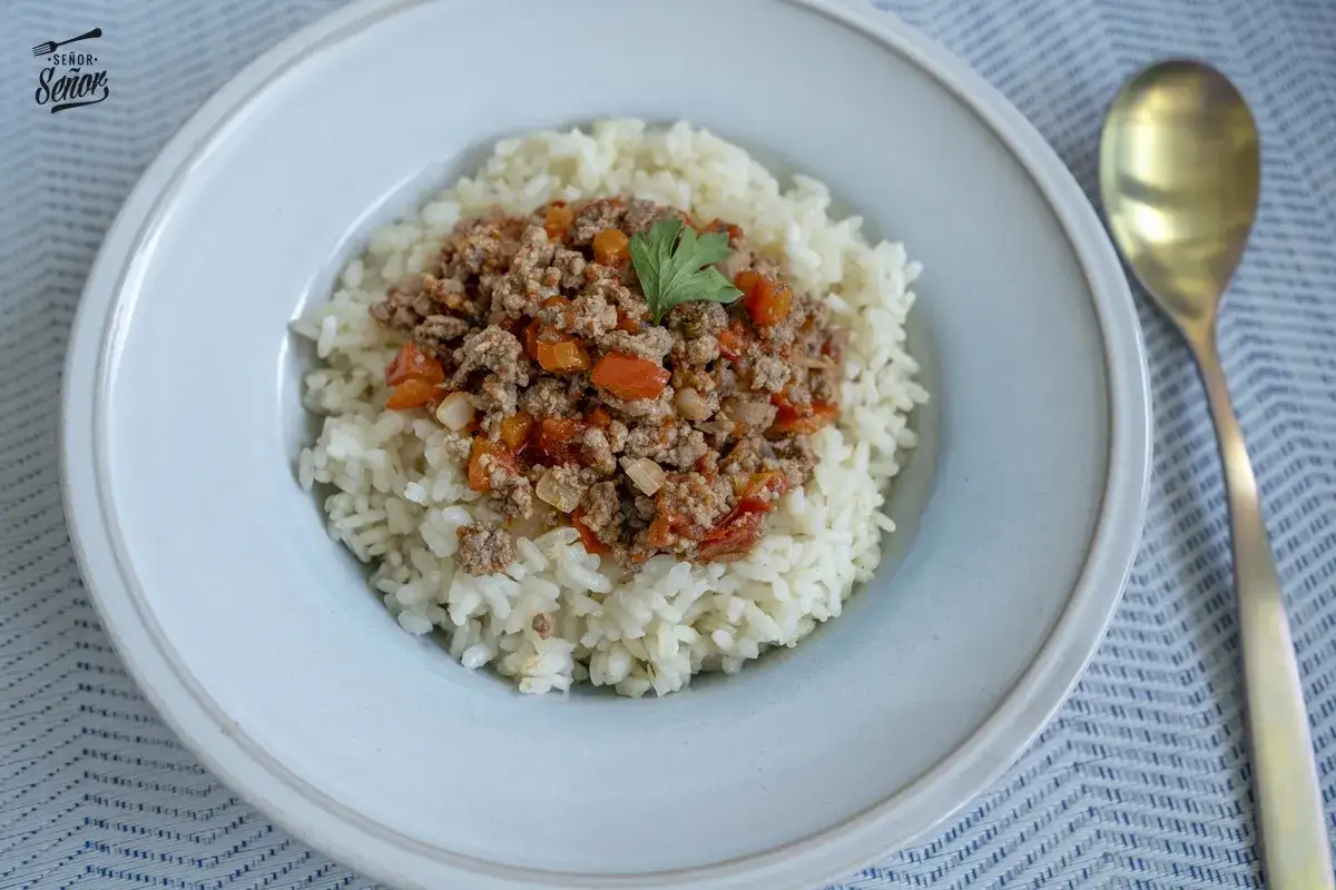 Plato de arroz blanco cubierto con una generosa porción de arroz con carne picada, adornado con una hoja de perejil.