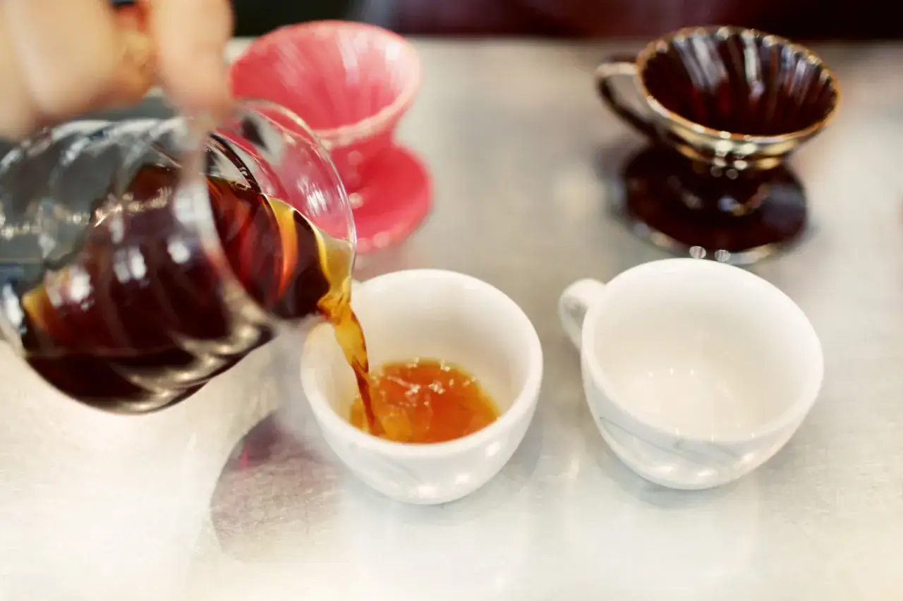 H&auml;r h&auml;lls nybryggt arabica kaffe i en vit kopp. Tv&aring; andra koppar och tv&aring; filterh&aring;llare syns i bakgrunden.