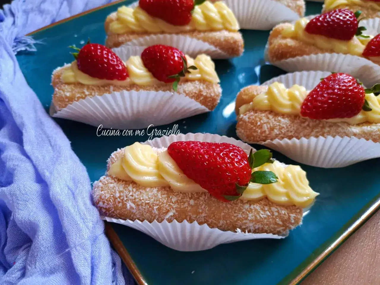 Deliziosi pasticcini con crema chantilly, fragole fresche e cocco grattugiato su un piatto blu.