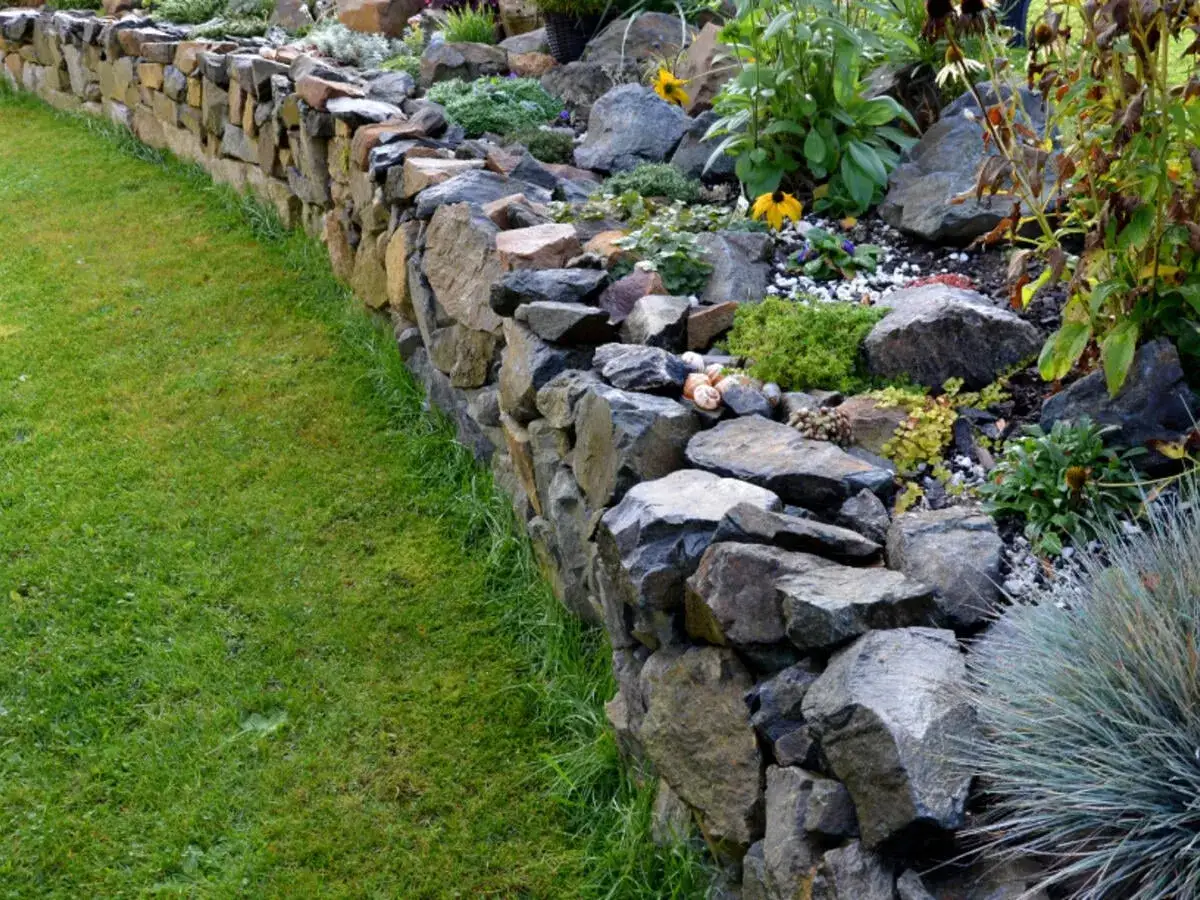 Eine kunstvoll errichtete Trockenmauer mit Steinen und Pflanzen, die einen Gartenbereich abgrenzt.