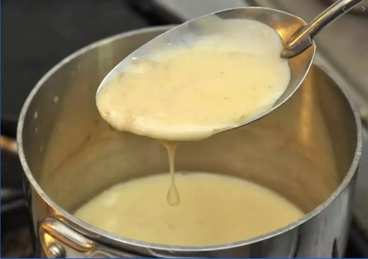 Une cuill&egrave;re de sauce onctueuse, pr&ecirc;te pour une recette de beurre blanc. La sauce coule doucement dans la casserole.