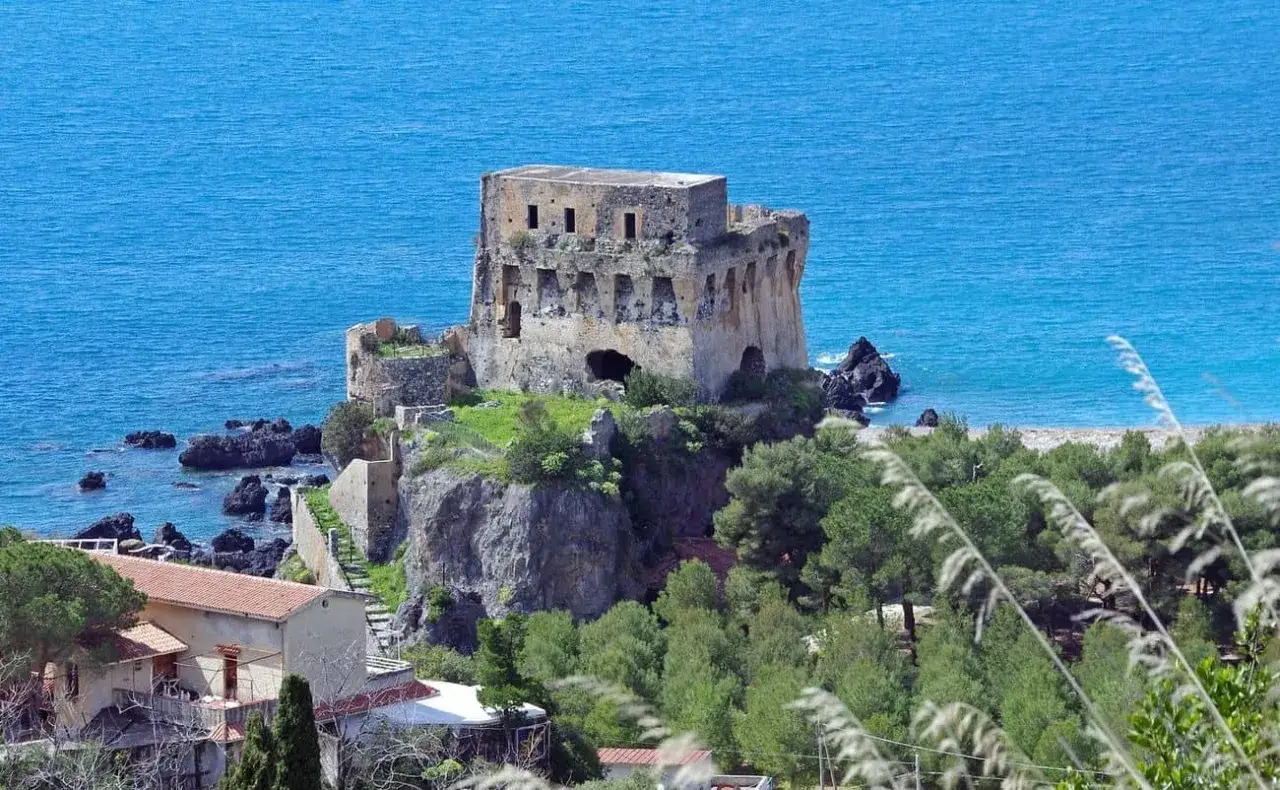 Torre aragonese a picco sul mare, uno dei borghi da visitare in Calabria, con case e vegetazione mediterranea.