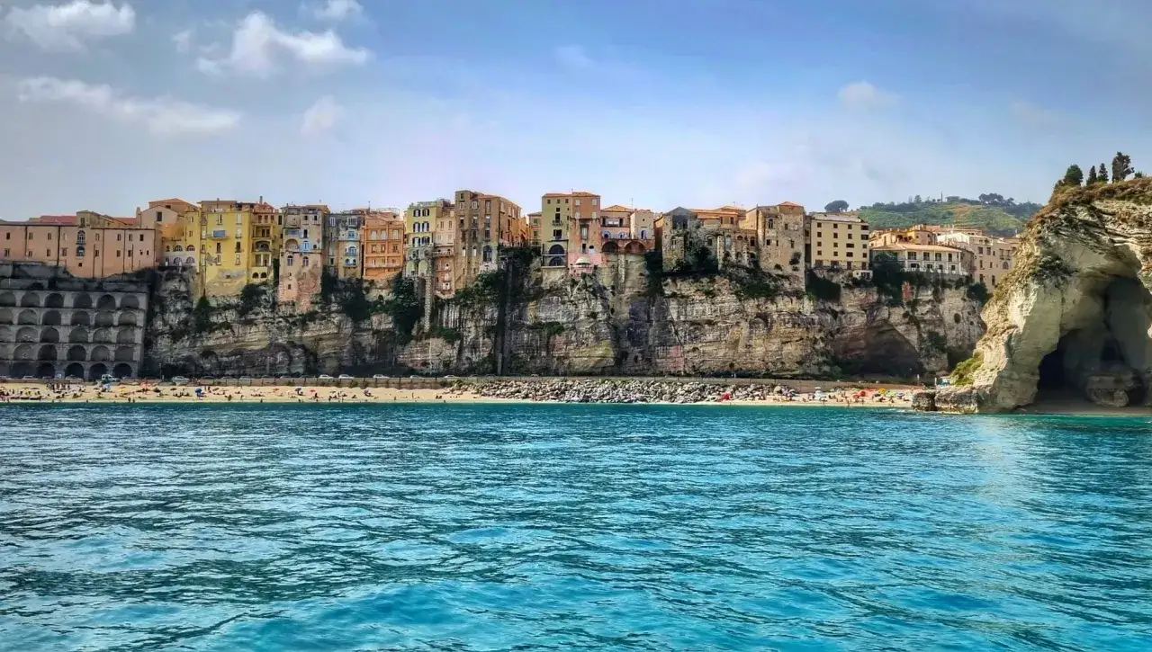 Case colorate a picco sul mare, una spiaggia affollata e un'onda azzurra. Un sogno che parte da Napoli e arriva a Tropea.