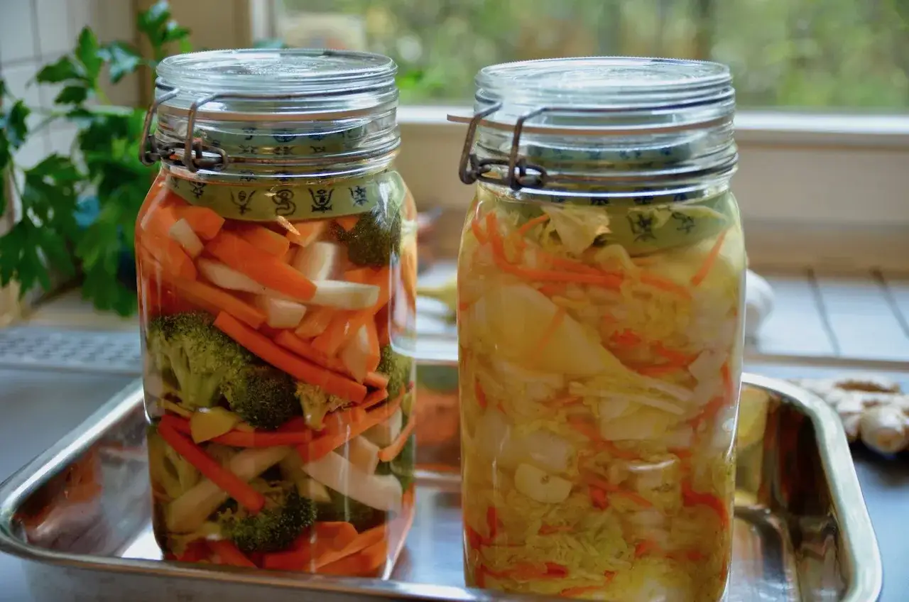 Zwei Gläser mit eingelegtem Gemüse, bereit für die Fermentation. So macht man Kimchi: Kohl, Karotten, Rettich und Brokkoli in Salzlake.