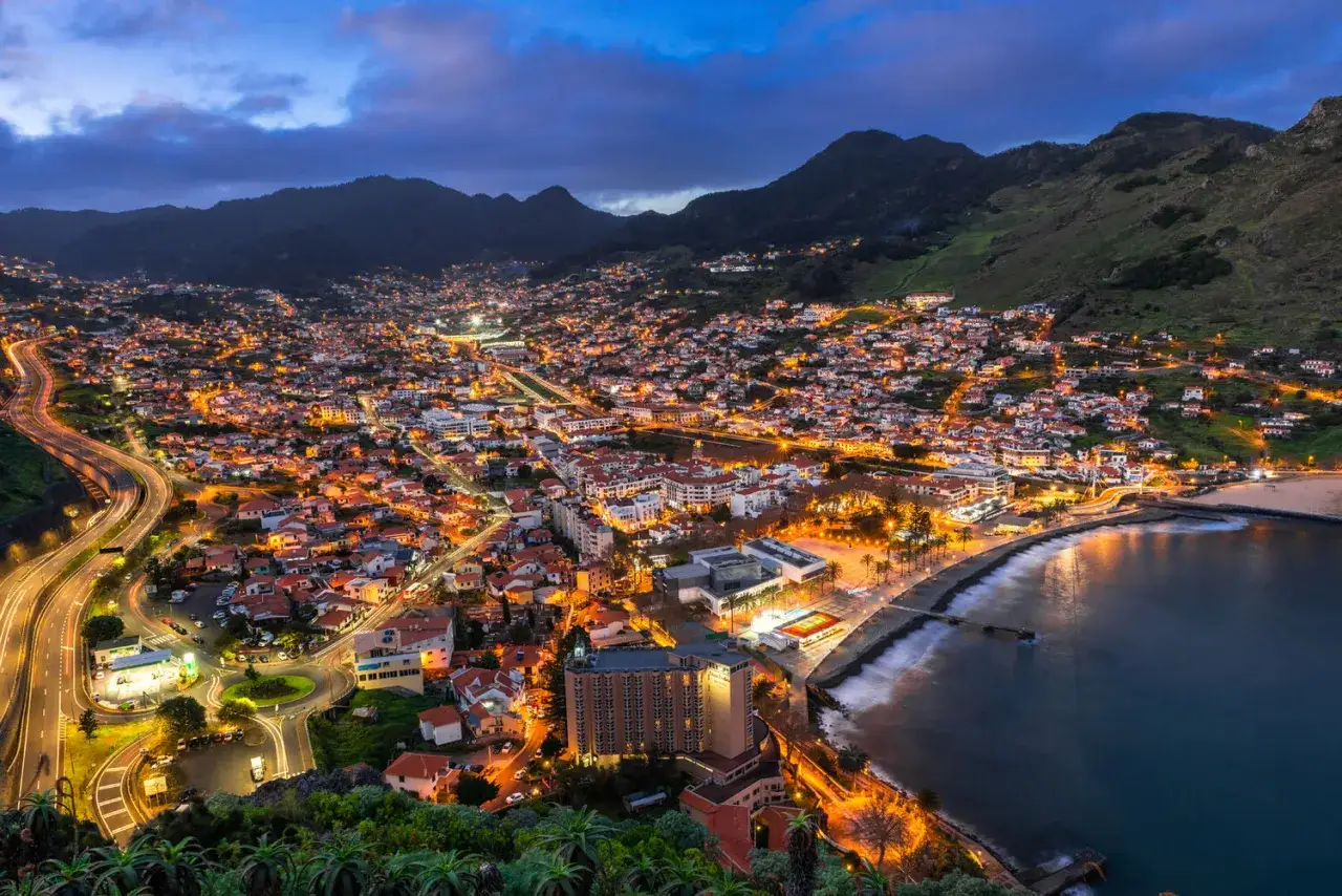 Lichtermeer in Machico, Madeira. Die Stadt erstreckt sich bergauf, beleuchtet von tausenden Lichtern, während die Wellen sanft an die Küste schlagen.
