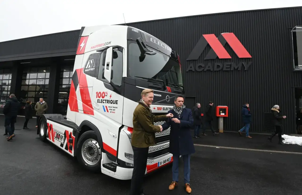 Deux hommes se serrent la main devant un camion &eacute;lectrique 100% MAUFFREY, PTAC 44T, devant le b&acirc;timent 