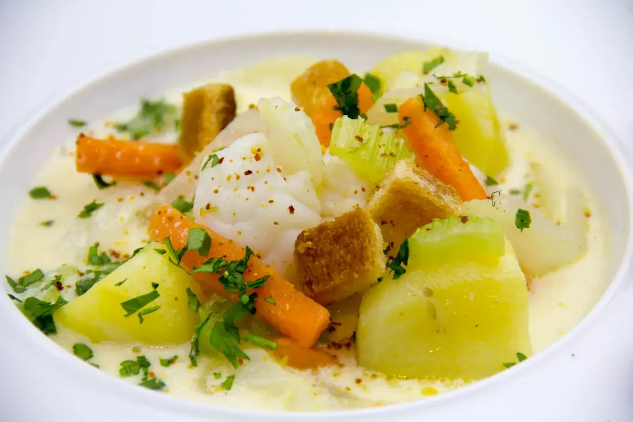 Bourride de lotte : morceaux de poisson blanc, carottes, pommes de terre, céleri et croûtons dans une sauce crémeuse, parsemée de persil frais.