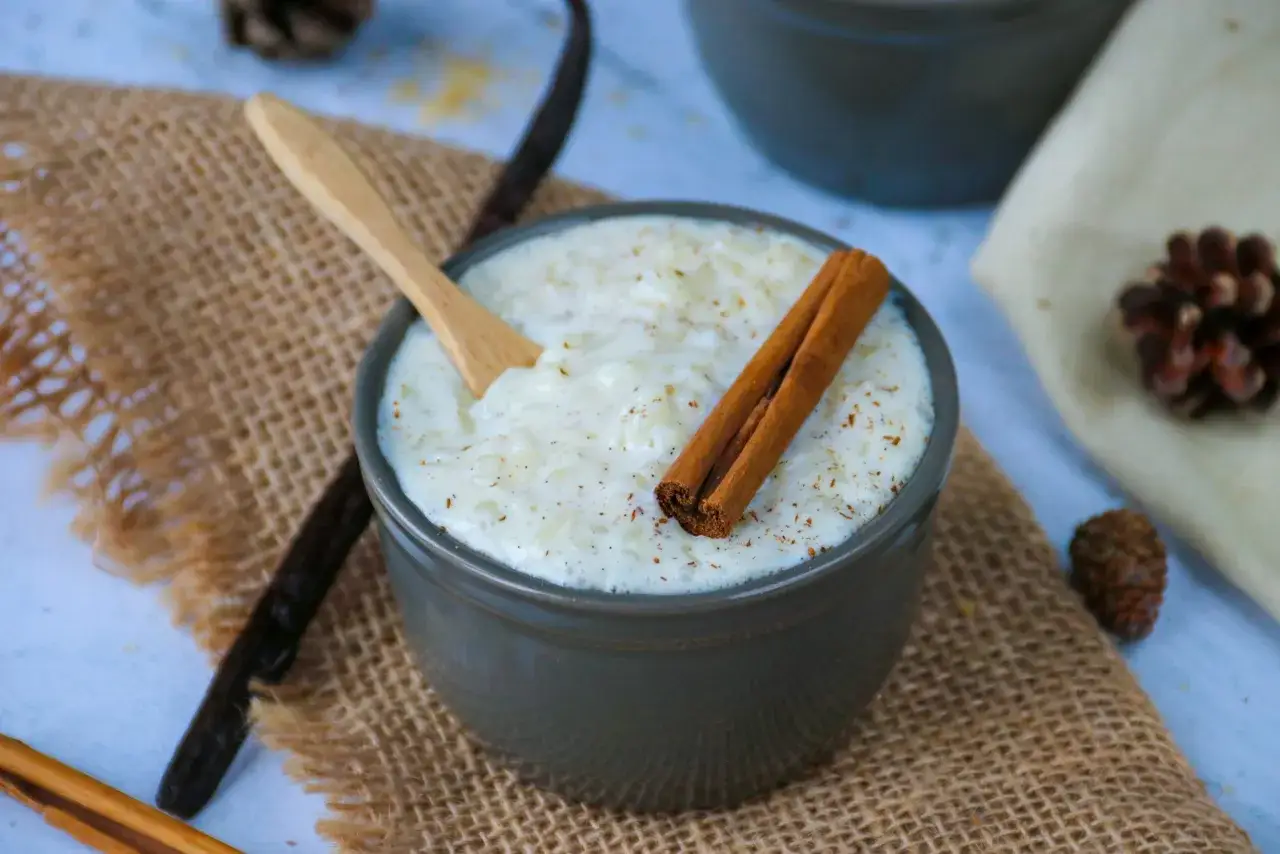 Un bol de riz au lait crémeux, garni de bâtons de cannelle et d'une cuillère en bois, sur un fond rustique avec des pommes de pin.