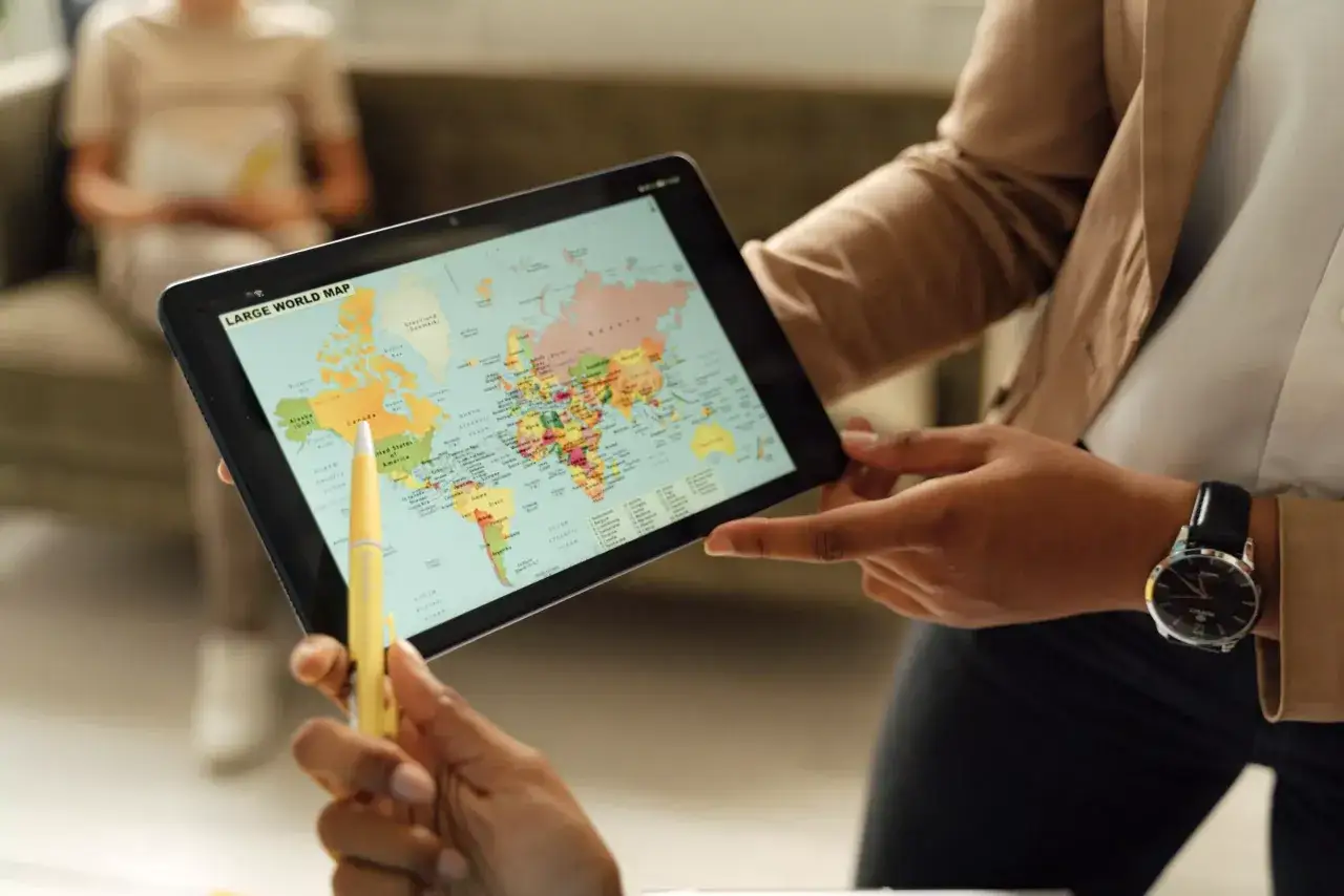 Eine Lehrkraft erklärt den Globus auf einem Tablet. Der **Erdkundeunterricht** beginnt mit einer Reise um die Welt.