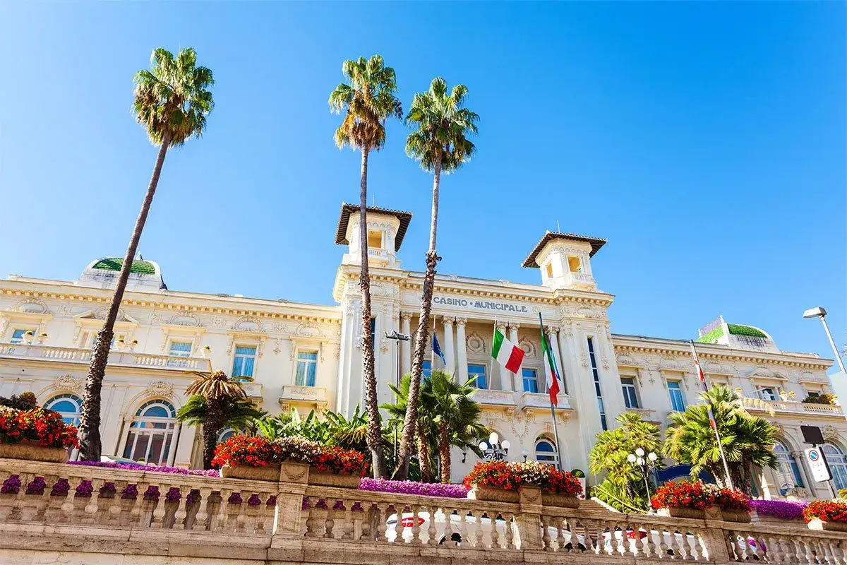 Casino Municipale w San Remo, miejsce słynnego festiwalu, otoczone palmami i kwitnącymi kwiatami.