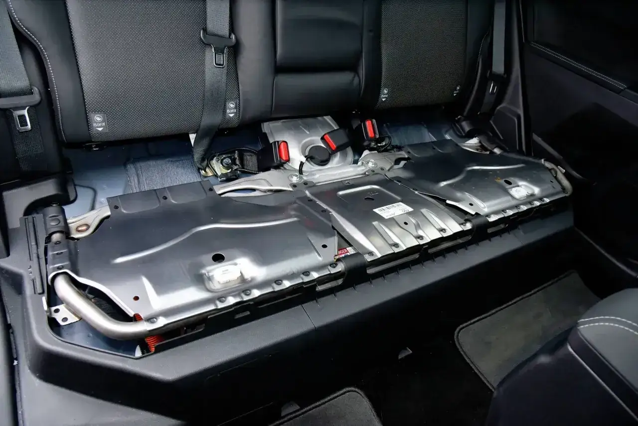 Podłoga pod tylnymi siedzeniami Toyoty Yaris Hybrid, odsłaniająca metalowe osłony. Tu znajduje się akumulator 12V.