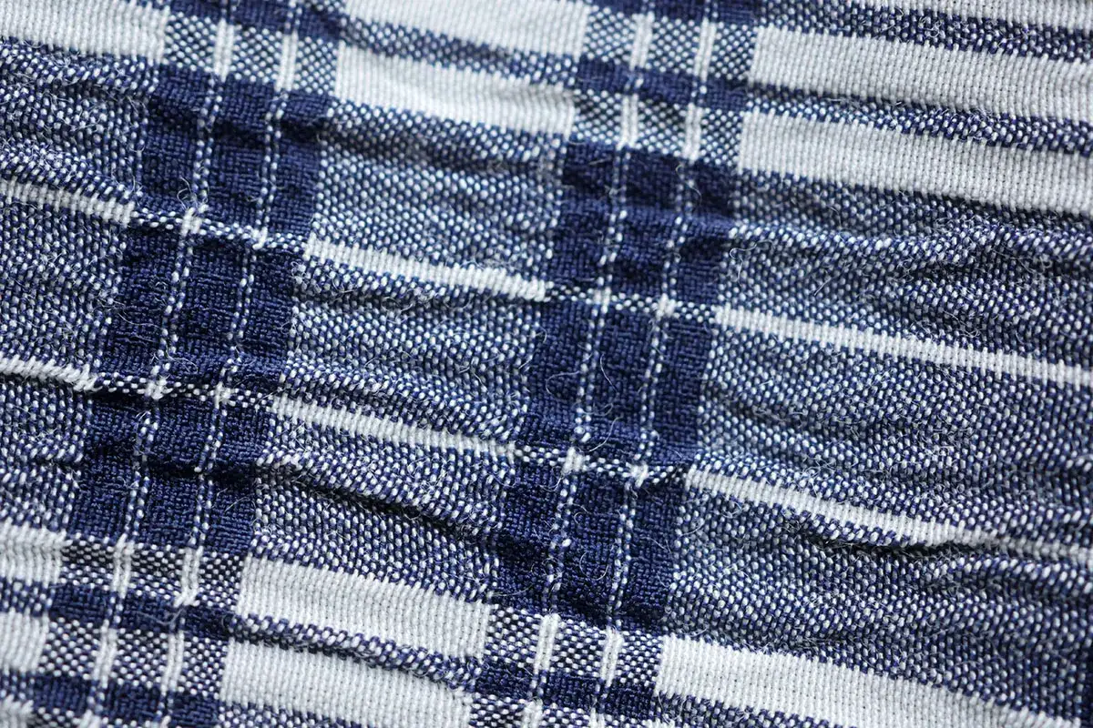 Nahaufnahme eines blauen und wei&szlig;en karierten Stoffes. Die Textur ist leicht zerknittert, was typisch f&uuml;r Seersucker ist.