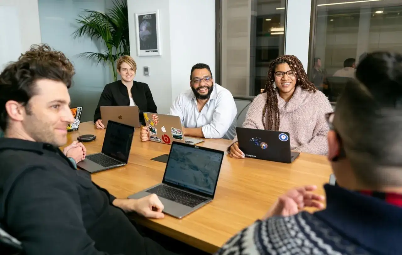 Een team bespreekt ideeën rond een tafel, laptops open. Dit is een voorbeeld van gedeeld leiderschap in het onderwijs, waar iedereen bijdraagt.