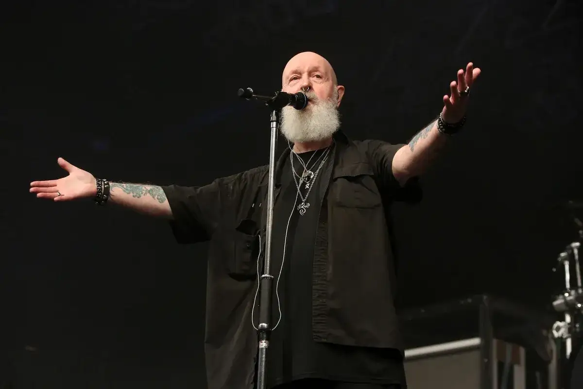 Rob Halford, der offen schwul ist, singt mit ausgestreckten Armen und Bart.