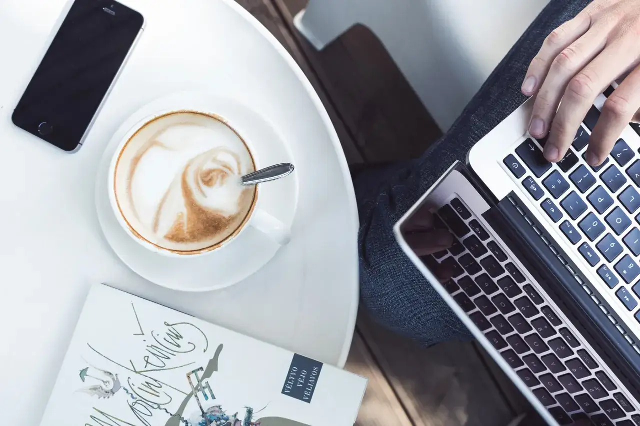 Person lernt im Caf&eacute; mit Laptop, Kaffee und Handy.