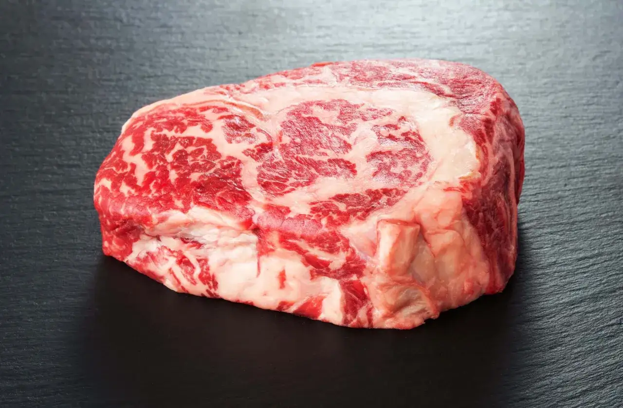 Ein rohes Rib Eye Steak mit feiner Marmorierung liegt auf dunklem Stein.
