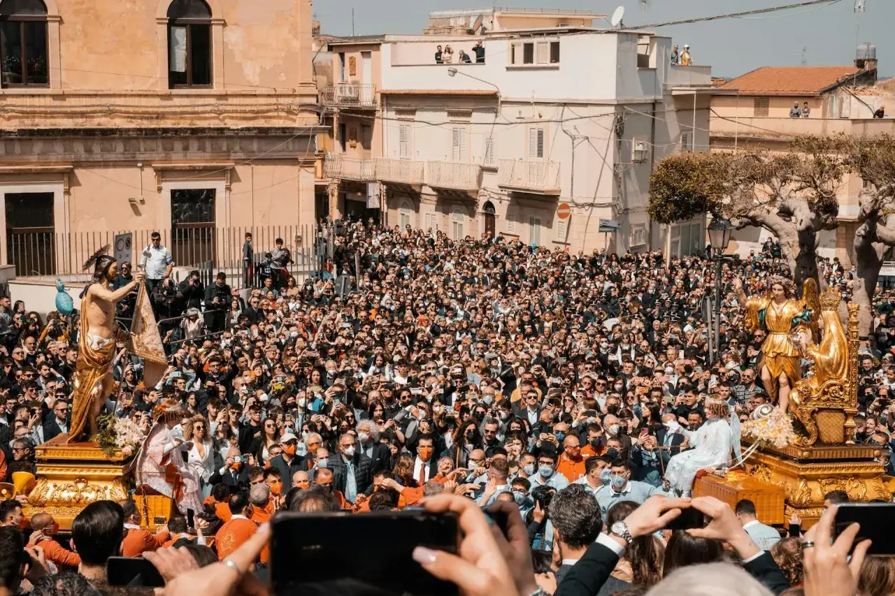 Folla immensa partecipa a una processione religiosa, un momento sentito quando si festeggia Pasqua. Statue dorate e fedeli creano un'atmosfera solenne.