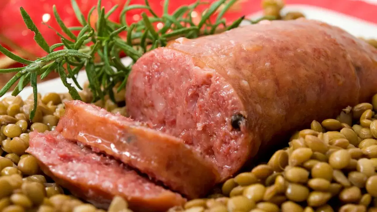 Un succulento cotechino affettato su un letto di lenticchie, guarnito con rosmarino. Un classico piatto di lenticchie e cotechino alla marchigiana.
