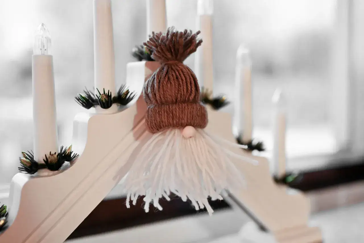 S&ouml;t tomte av toarullar med brun m&ouml;ssa och vitt sk&auml;gg, sitter p&aring; en ljusstake med elektriska ljus.