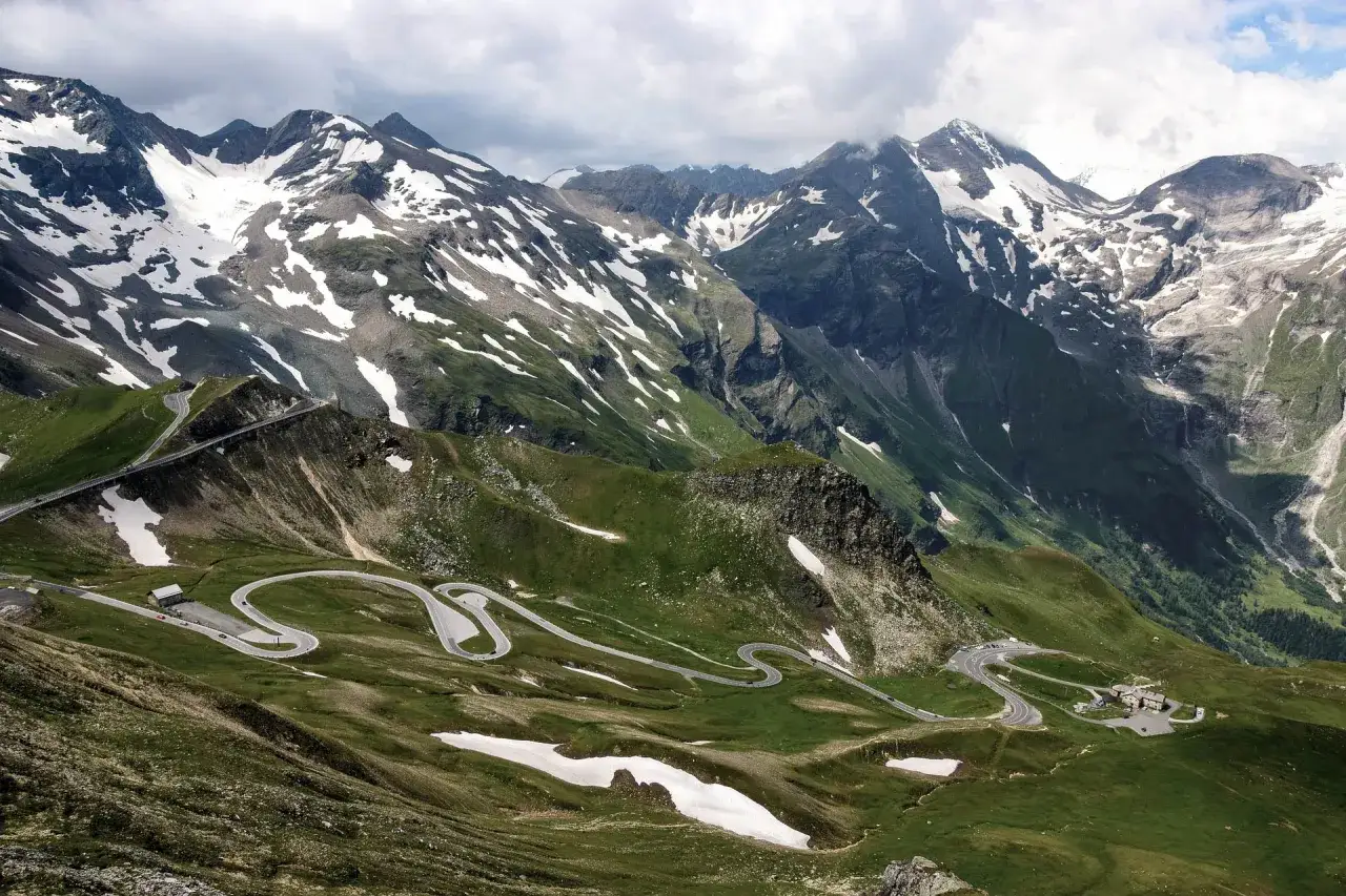 Kręta droga w Alpach, idealna na alpejski grand tour. Majestatyczne szczyty górskie, częściowo pokryte śniegiem, otaczają zielone zbocza.