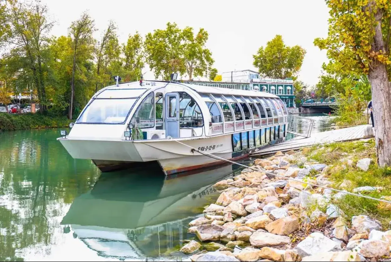 Barco turístico en el río Tajo, ideal para saber qué ver en Aranjuez con niños. Reflejos verdes y piedras en la orilla.